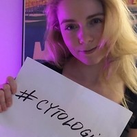 Kolorowe zdjęcie. Kobieta trzyma w dłoniach białą kartkę papieru z napisem: #cytologia