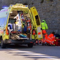 Kolorowa fotografia. Ratownicy medyczni udzielają pomocy rannemu. Obok na poszkodowanego czeka karetka pogotowia.