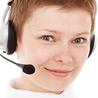 Kolorowa fotografia. Uśmiechnięta kobieta ze słuchawkami na uszach i mikrofonem.