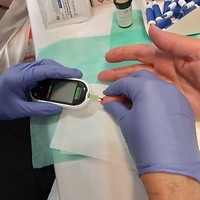 Kolorowa fotografia. Trwa badanie poziomu cukru we krwi. Pasek w glukometrze dotyka kropli krwi na palcu.