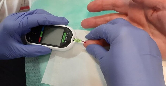 Kolorowa fotografia. Trwa badanie poziomu cukru we krwi. Pasek w glukometrze dotyka kropli krwi na palcu.