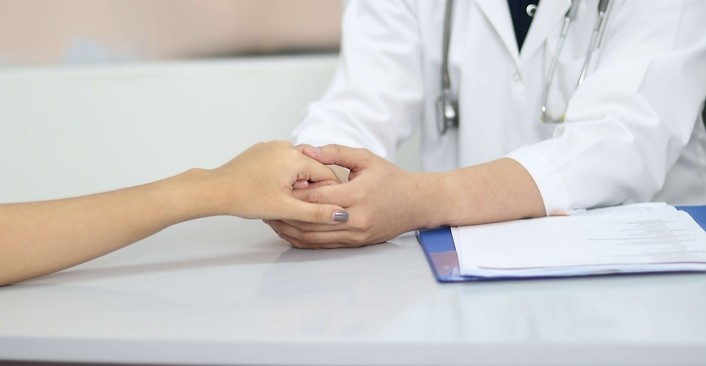 Kolorowa fotografia. Lekarz ubrany w biały fartuch trzyma za dłoń pacjentkę.
