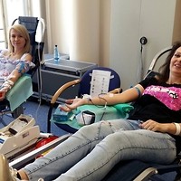 Kolorowa fotografia. Mobilny punkt poboru krwi w siedzibie Centrali NFZ. Krew pobierana jest od dwóch pracowników NFZ