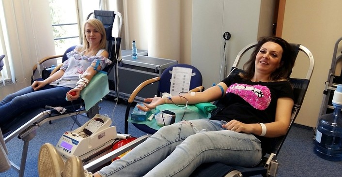 Kolorowa fotografia. Mobilny punkt poboru krwi w siedzibie Centrali NFZ. Krew pobierana jest od dwóch pracowników NFZ