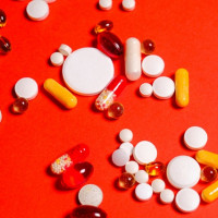 Kolorowa fotografia. Różnego rodzaju tabletki i leki na czerwonym tle.