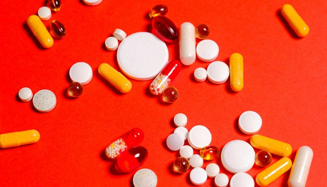 Kolorowa fotografia. Różnego rodzaju tabletki i leki na czerwonym tle.